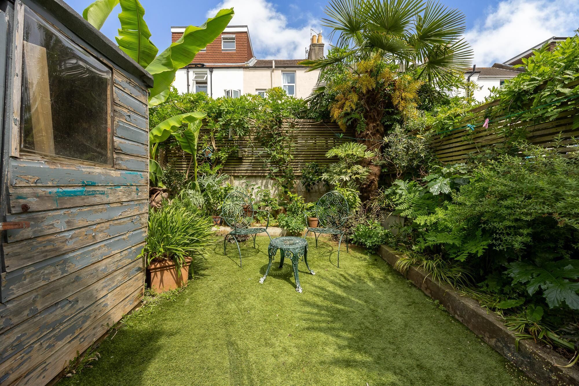 Un jardin avec un abri en bois, une table en métal et des chaises.