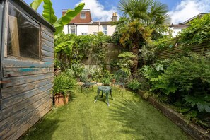 Un jardin avec un abri en bois, une table en métal et des chaises.