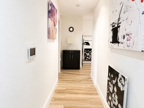 A hallway with a wooden floor, a black cabinet, and a wall-mounted light fixture. - River Views | 2BR 2BA | Roof Terrace + Parking - Pass the Keys (London)