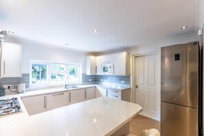 A modern kitchen with a central island, stainless steel appliances, and a view of greenery outside. - Luxury 4-Bedroom house near Southend - Pass the Keys (Southend-on-Sea)