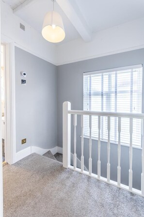 A room with a grey carpet, white walls, a white railing, and a window with blinds. - Luxury 4-Bedroom house near Southend - Pass the Keys (Southend-on-Sea)