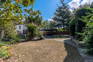 A backyard with a patio, a pergola, and a variety of trees and shrubs. - Luxury 4-Bedroom house near Southend - Pass the Keys (Southend-on-Sea)