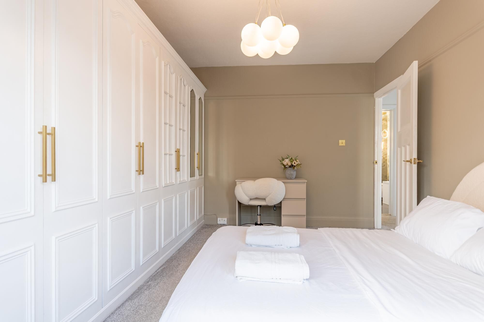 A hotel room with a large bed, a vanity with a mirror, and a hanging light fixture.