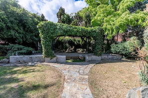 A garden with a stone pathway, a covered seating area, and various plants. - Luxury 4-Bedroom house near Southend - Pass the Keys (Southend-on-Sea)