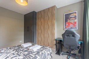 A hotel room with a bed, a desk, a chair, a wardrobe, and a poster on the wall. - Luxury 4-Bedroom house near Southend - Pass the Keys (Southend-on-Sea)
