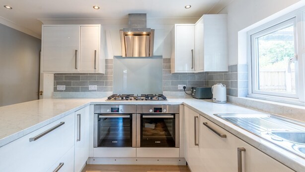 A modern kitchen with stainless steel appliances, white cabinetry, and a window providing natural light. - Luxury 4-Bedroom house near Southend - Pass the Keys (Southend-on-Sea)