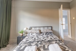 Un dormitorio con cama, mesita de noche, lámpara y una planta en maceta.