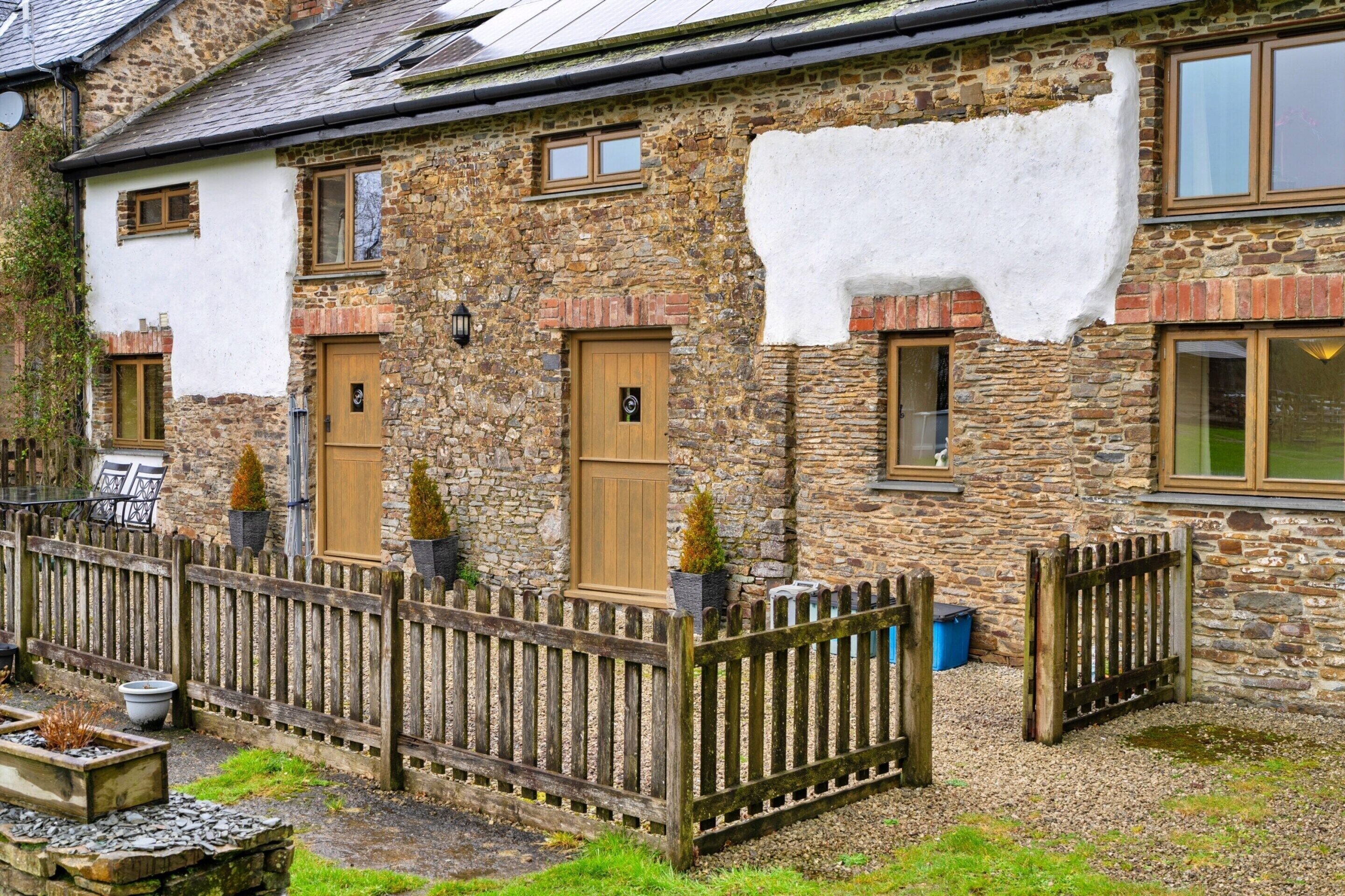 A stone house with a white exterior, wooden doors, and a wooden fence.