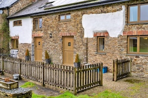 A stone house with a white exterior, wooden doors, and a wooden fence.