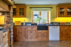 A kitchen with wooden cabinets, a stone wall, a built-in oven, and a dishwasher.