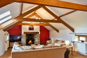 A cozy loft-style living room with a stone fireplace, wooden beams, and a television.