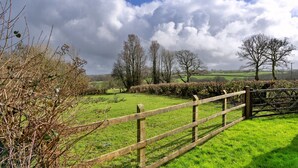 A rural landscape with a wooden fence, green fields, and trees under a cloudy sky. - Inviting Holiday Cottage in Beaworthy (Beaworthy)