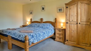 A bedroom with a wooden bed, bedside lamps, a wooden wardrobe, and two framed pictures on the wall. - Inviting Holiday Cottage in Beaworthy (Beaworthy)