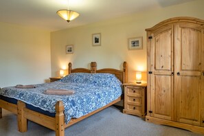 Quarto com cama de madeira, luminárias de cabeceira, guarda-roupa de madeira e duas imagens emolduradas na parede.