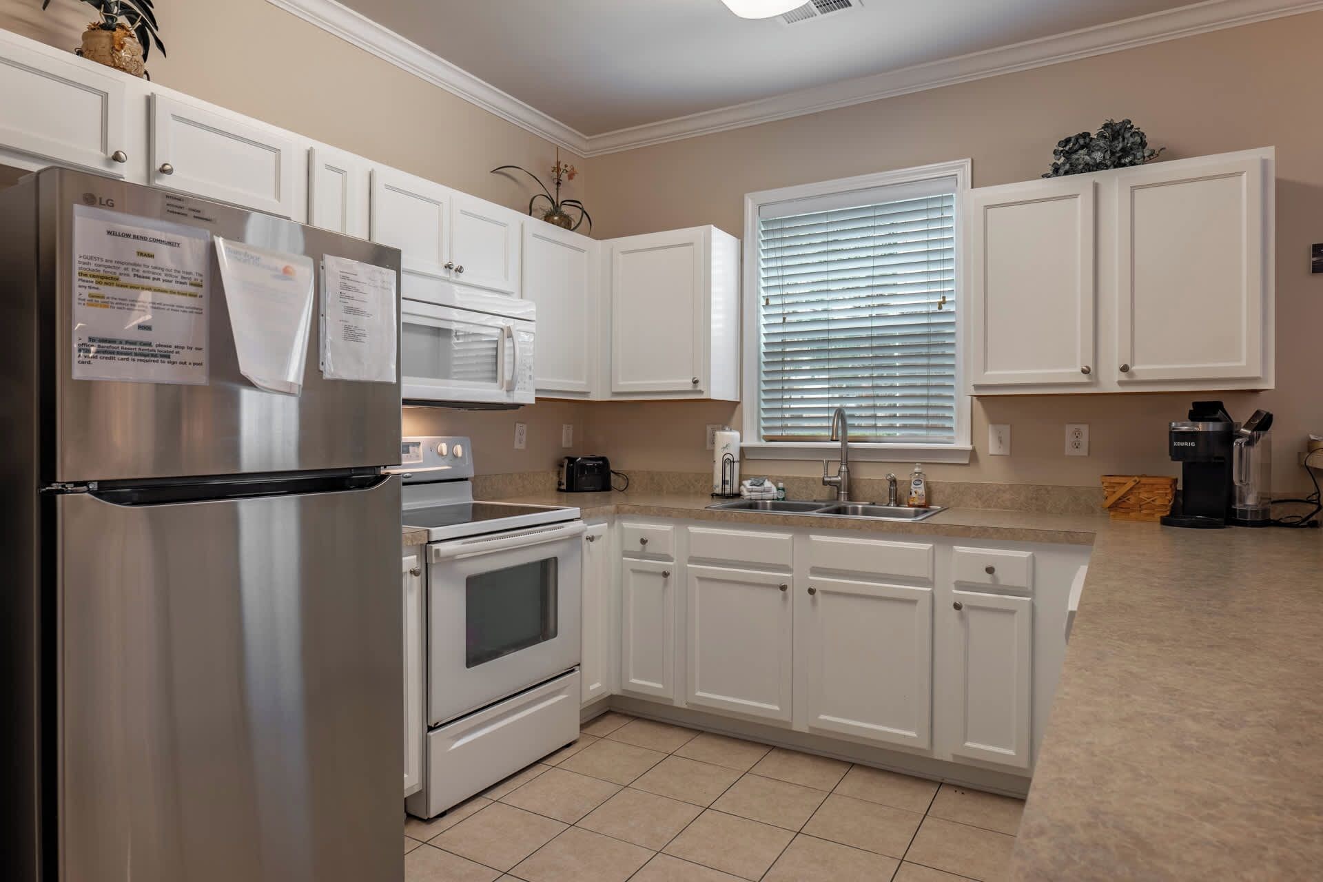 A kitchen with white cabinets, a stainless steel refrigerator, a microwave, an oven, and a sink.