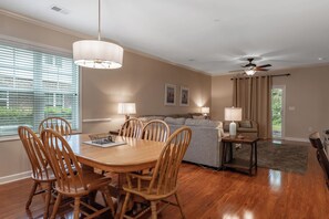 A dining area with a wooden table and chairs, a ceiling fan, and a sofa in the background. - Willow Bend At Barefoot 1111 (North Myrtle Beach)