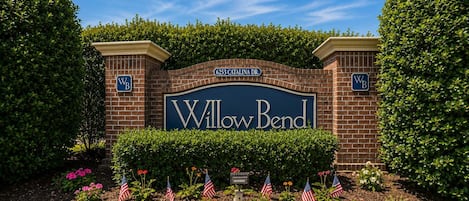 Une enseigne pour Willow Bend, avec une arche en briques, entourée de haies taillées et de drapeaux américains.