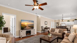 Ein Wohnzimmer mit Kamin, Deckenventilator und Fernseher, der eine Strandansicht zeigt.