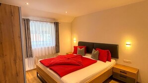 Ein modernes Schlafzimmer mit einem hölzernen Bett, einem Nachttisch und einem Fenster mit Vorhängen.