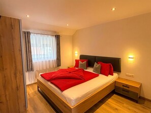 Ein modernes Schlafzimmer mit einem hölzernen Bett, einem Nachttisch und einem Fenster mit Vorhängen.