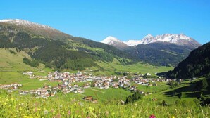 Ein Bergdorf mit Häusern und einer Kirche, umgeben von grünen Feldern und Bergen.