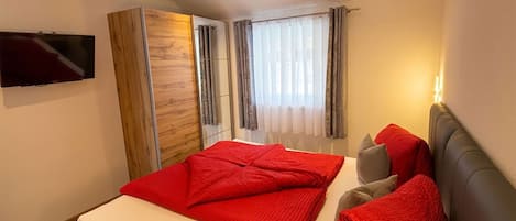 Un dormitorio moderno con una cama grande, un armario, un televisor de pantalla plana y una ventana con cortinas.