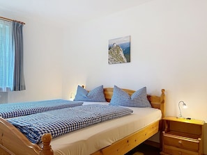 Ein Einzelbett mit karierter Bettwäsche, ein Holzkopfende, ein Nachttisch mit Lampe und ein Wandbild.