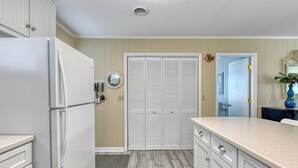 A kitchen with a refrigerator, white cabinets, a wooden floor, and a door with a mirror. - Sail Away - 4 Bedroom, 2.5 Bath Beach Home - Dog Friendly with Fenced In Yard (Garden City Beach)