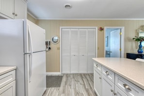 A kitchen with a refrigerator, white cabinets, a wooden floor, and a door with a mirror. - Sail Away - 4 Bedroom, 2.5 Bath Beach Home - Dog Friendly with Fenced In Yard (Garden City Beach)
