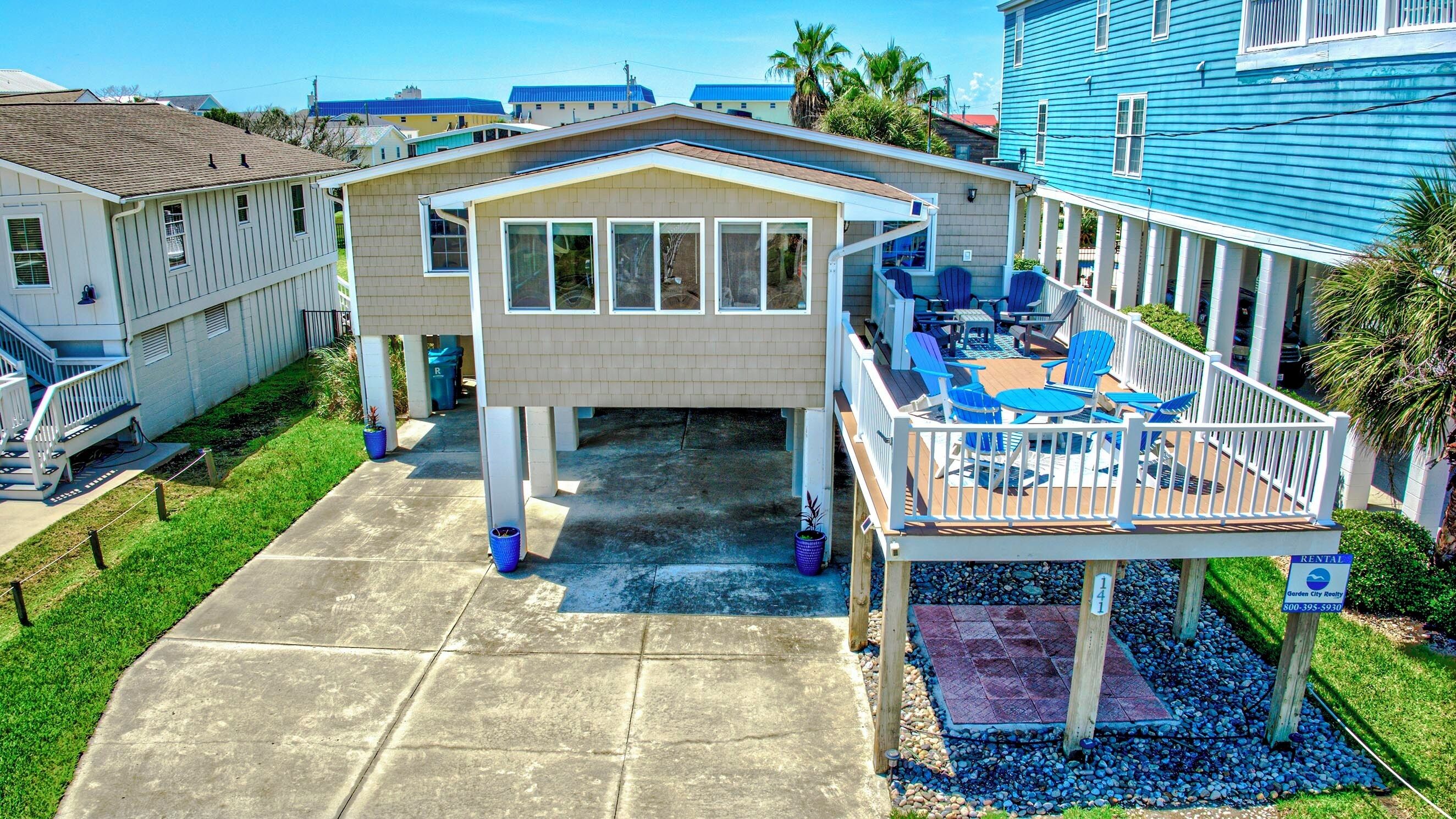 Ein zweistöckiges Haus mit überdachter Terrasse und kleiner Holzterrasse.