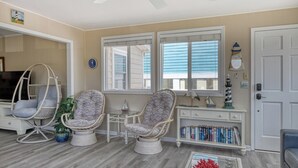 A room with a television, two wicker chairs, a small table, a bookshelf, and a door. - Sail Away - 4 Bedroom, 2.5 Bath Beach Home - Dog Friendly with Fenced In Yard (Garden City Beach)