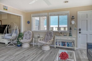 A room with a television, two wicker chairs, a small table, a bookshelf, and a door. - Sail Away - 4 Bedroom, 2.5 Bath Beach Home - Dog Friendly with Fenced In Yard (Garden City Beach)