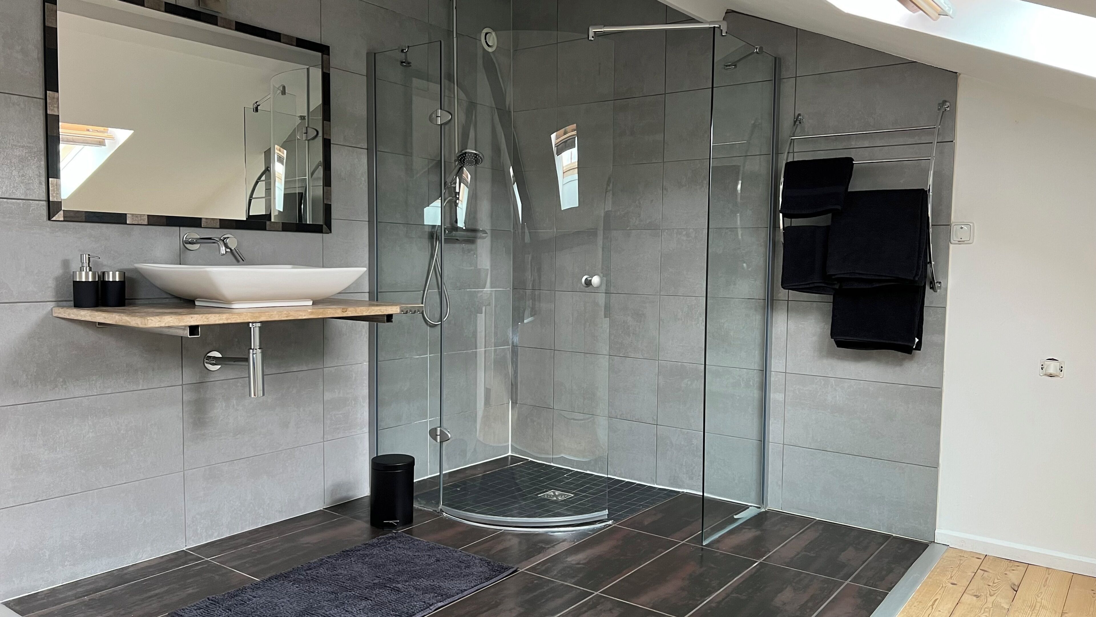 Een moderne badkamer met een douche met glazen wand, een wastafel op voetstuk en een spiegel boven de wastafel.
