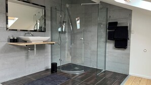 Een moderne badkamer met een douche met glazen wand, een wastafel op voetstuk en een spiegel boven de wastafel.