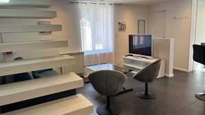 Een moderne woonkamer met een flatscreen televisie, een salontafel en twee stoelen.