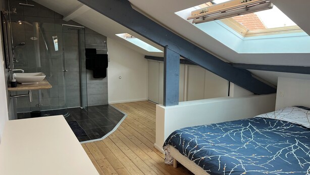 Een slaapkamer met dakraam, douche en een bed met een beddengoed met patroon.
