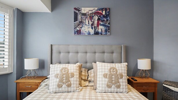 A bedroom with a checkered bedspread, two nightstands with lamps, and a painting above the bed. - Amazing Holiday Home Near London Airport (Hounslow)