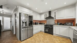 A modern kitchen with stainless steel appliances, white cabinetry, and a herringbone wood floor. - Amazing Holiday Home Near London Airport (Hounslow)