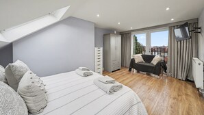 A bedroom with a bed, a dresser, a TV, and a balcony with a view. - Amazing Holiday Home Near London Airport (Hounslow)