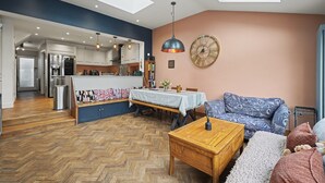 A modern living room with a herringbone floor, a wooden coffee table, a patterned sofa, and a dining area with a table and chairs. - Amazing Holiday Home Near London Airport (Hounslow)