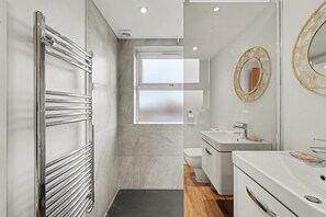 Uma casa de banho moderna com cabine de chuveiro em vidro, sanita, lavatório com espelho e toucador.