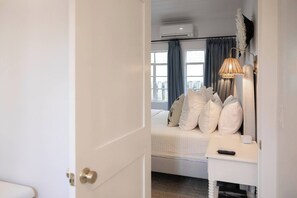 A bedroom with a bed, bedside table, lamp, and an air conditioning unit.