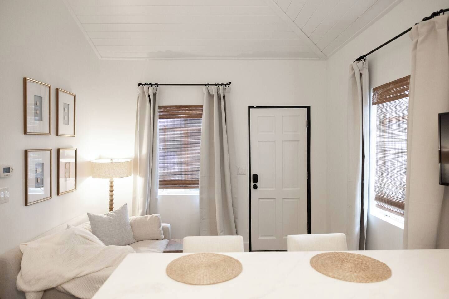 Une pièce avec une porte blanche, une table avec deux sets de table, un canapé avec des coussins et une lampe.
