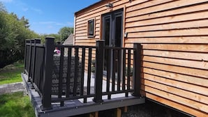A wooden cabin with a black metal railing, a door, and a small window. - Min yr Afon Cabin Sleeps2 Hot Tub Parking (Holyhead)