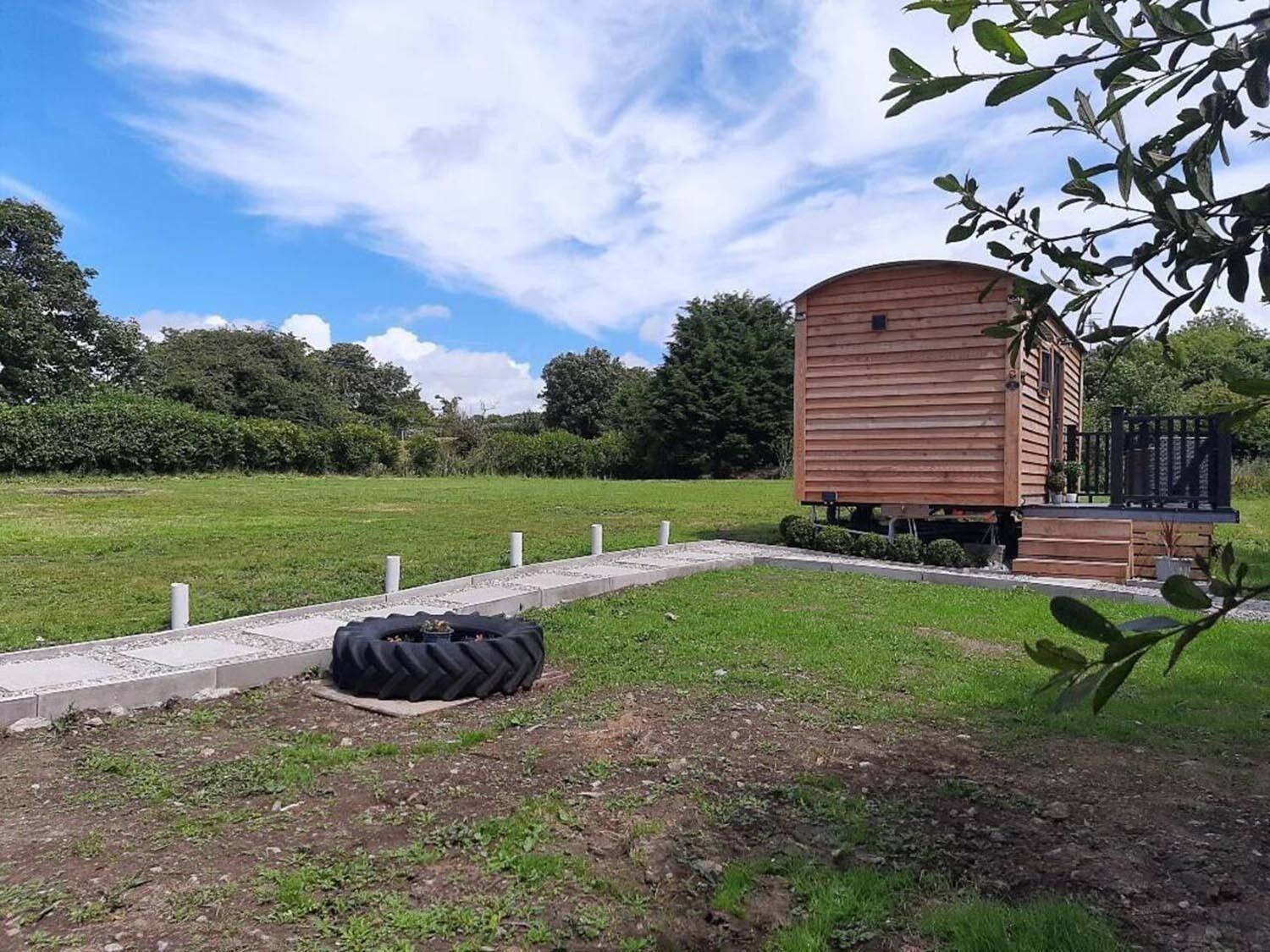 Una cabaña de madera con un porche, rodeada de un campo de pasto y árboles.