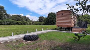 Una cabaña de madera con un porche, rodeada de un campo de pasto y árboles.
