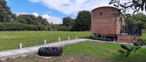 Une cabane en bois dotée d’un porche, entourée d’un champ verdoyant et d’arbres.