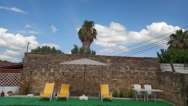 A stone wall with a palm tree, outdoor seating with yellow and white chairs, and a green lawn. - Green Palace-Guest House (Vale de Figueira)
