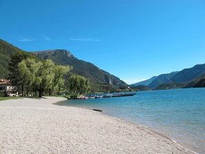 Ein Kiesstrand mit vertäuten Booten, ein Haus links und dahinter Berge.