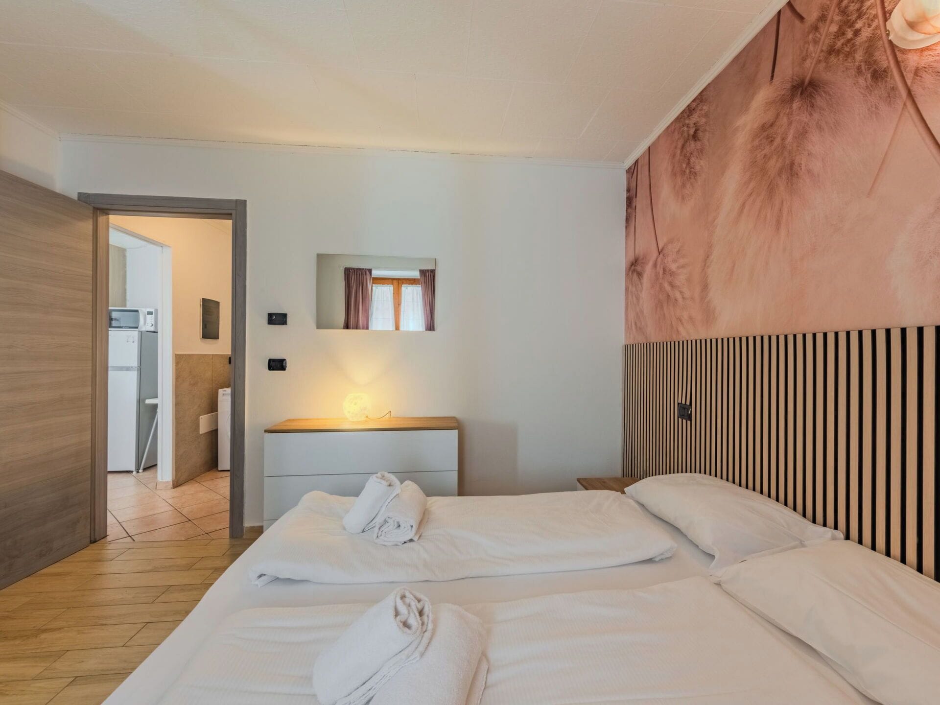 Ett hotellrum med två sängar, en sänggavel i trä, en spegel och utsikt över badrummet.